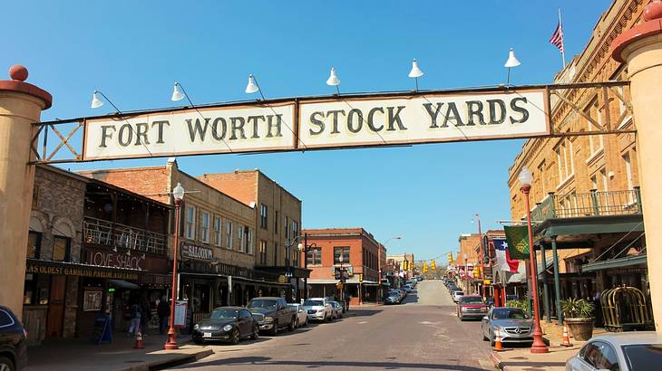 A sign that says "Fort Worth Stock Yards" over a street with cars and buildings on it