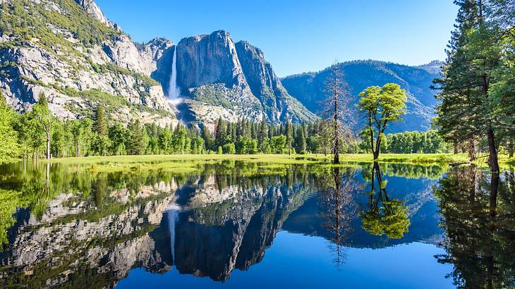 Mountains with greenery and a waterfall on them next to trees and a lake