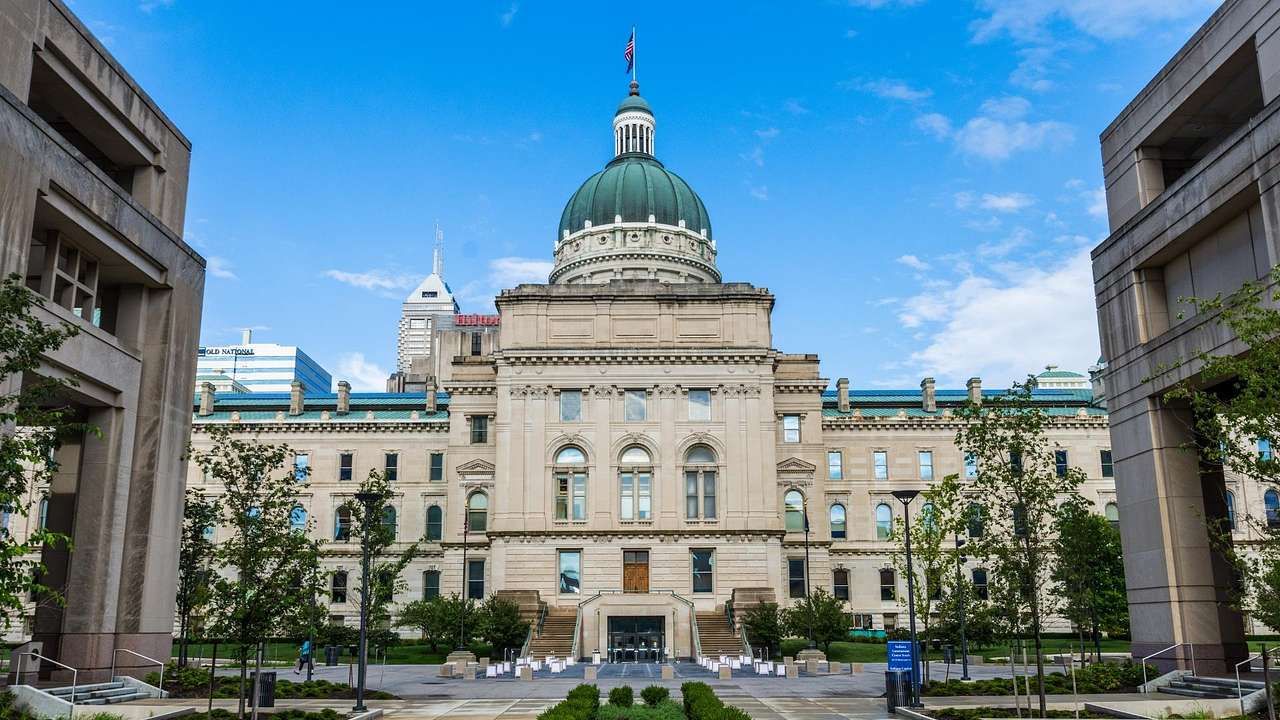 A stone state capitol building with a green-domed roof under a clear blue sky
