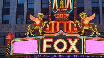 A neon sign on a theater that says "Fox" next to two lions with wings