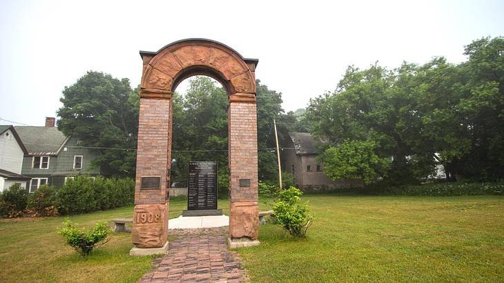 A tall, brown arched structure surrounded by grass and trees on a nice day