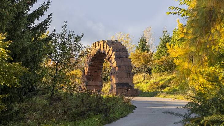 A walkway winding through green grass and trees with a stone arch sculpture