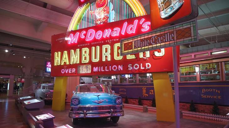A vintage blue car in front of a lit-up vintage McDonald's sign