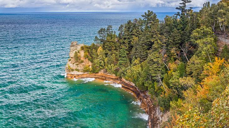 Aerial of a cliff covered with green trees overlooking a shoreline