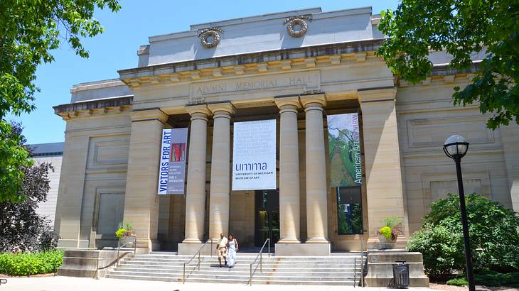 A neoclassical building with a staircase, and a street light & trees outside