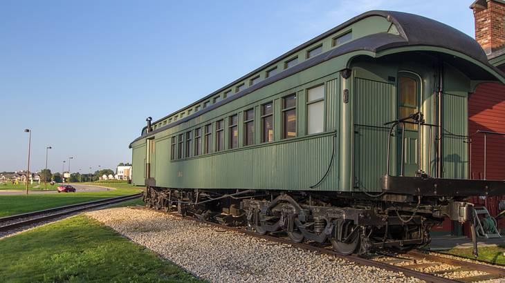 A dark green train car on a railway track, beside grass & under a clear sky