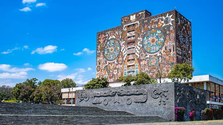 A building covered in a mural next to steps and greenery under a blue sky