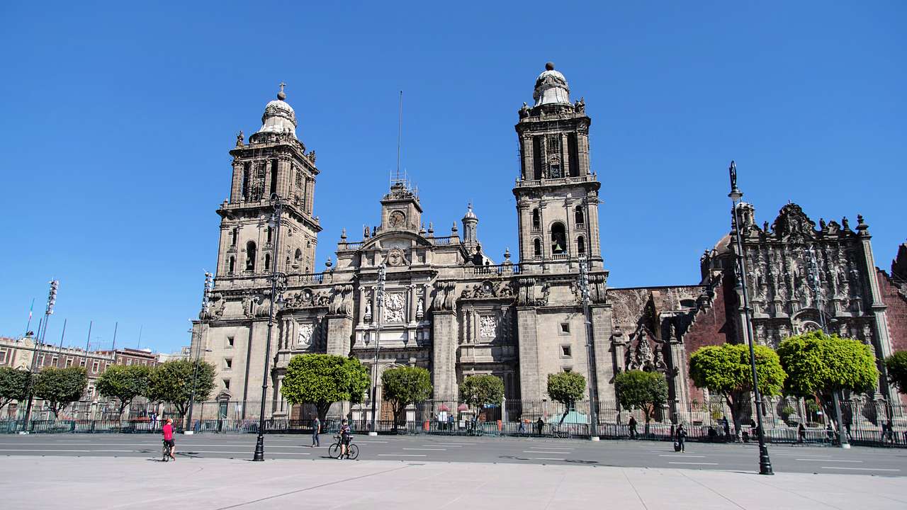 A cathedral with two towers, next to trees and a street under a blue sky