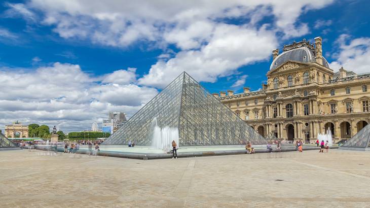 A large glass pyramid in the courtyard of a palace with tourists