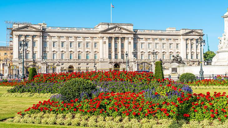 A lush garden of purple and red flowers in front of a white palace with a flag on top