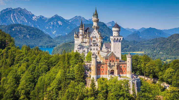 A fairytale castle with turrets surrounded by trees and mountains in the background