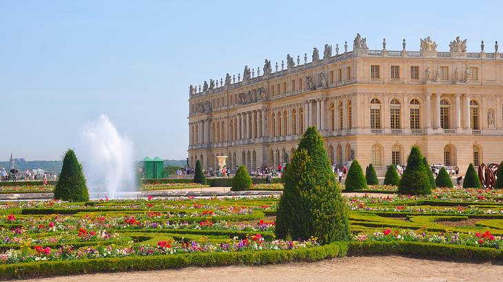 A palace with a fountain and a garden of flowers, cone-shaped trees, and a hedge maze