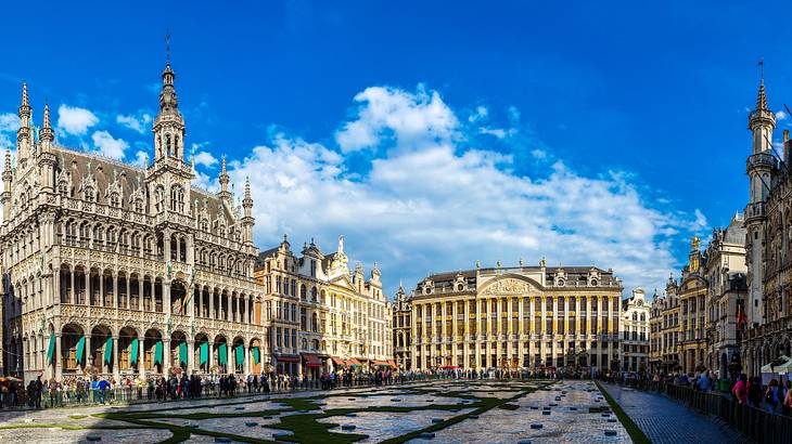 A cobbled square surrounded by Gothic buildings and people, under a partly cloudy sky