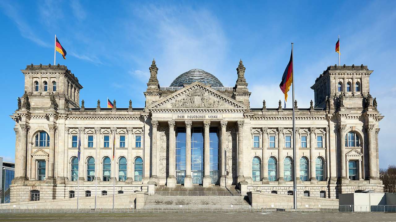 A large stone building with a dome made of glass and metal, and several flags