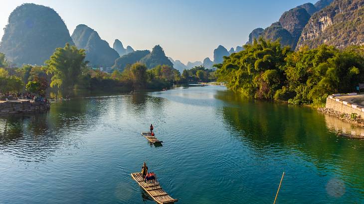 A large river with two bamboo rafts and trees lining up both sides on a nice day