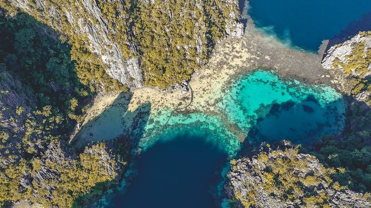 Aerial view of a turquoise lake amongst tall limestone rocks with greenery