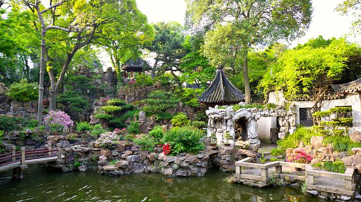A pond surrounded by a rock garden with trees, flowers, and small pagodas