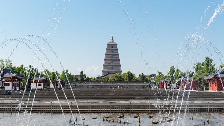 A square with many fountains with stairs leading to a tall, brick pagoda and trees