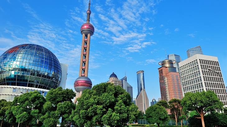 A tower with three purple spheres beside a glass-covered sphere, trees, and buildings