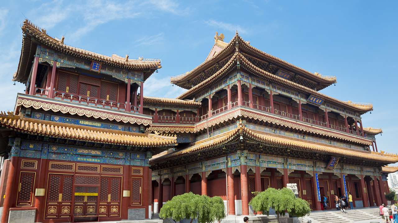 Two ancient temples with a maroon exterior and yellow roofs visited by tourists