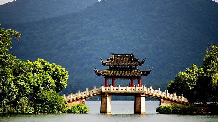 A river and bridge with a pavilion and people at the center, and trees on the sides