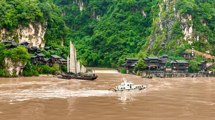 A long brown river with boats and old houses and trees lined up on its cliff banks