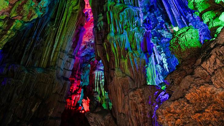 Walls and pillars of stone in an underground cave lit by colored lights