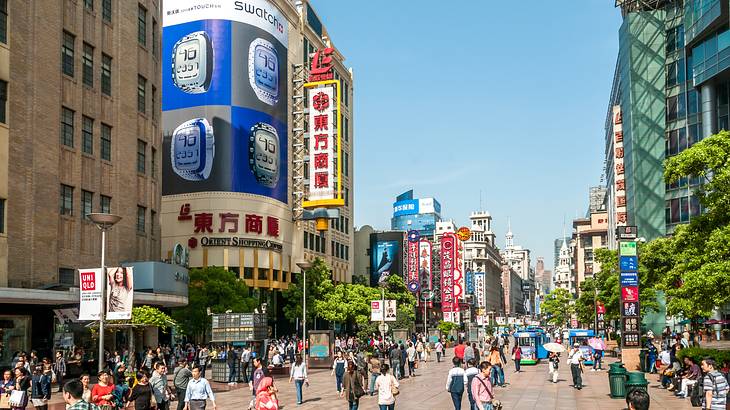 A long, wide road full of people and trolleys with buildings lined up on both sides