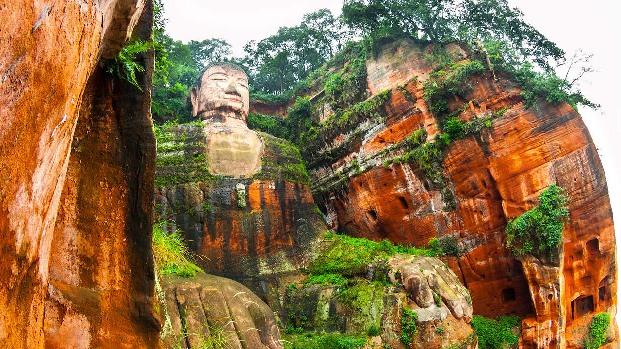 A giant stone Buddha in a seated position carved out of the side of a mountain