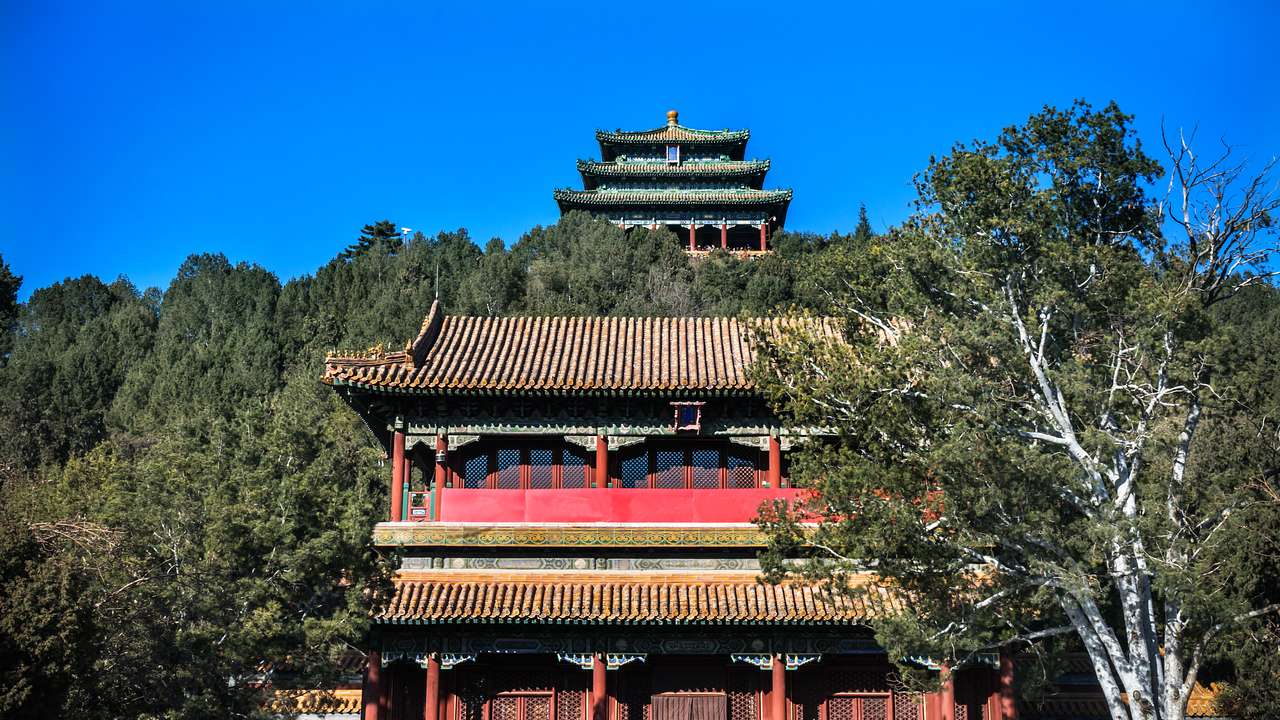 A temple on top of a hill surrounded by trees with a historical building below