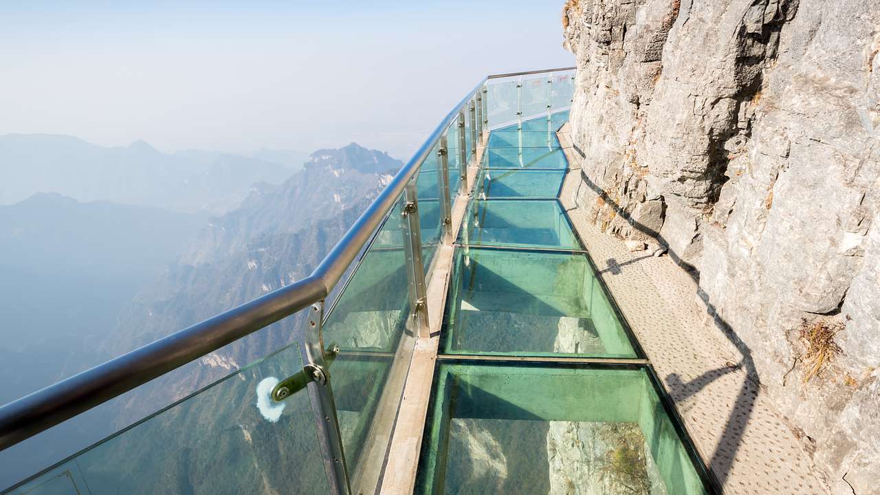 A glass walkway with steel railings along the side of a rocky mountain