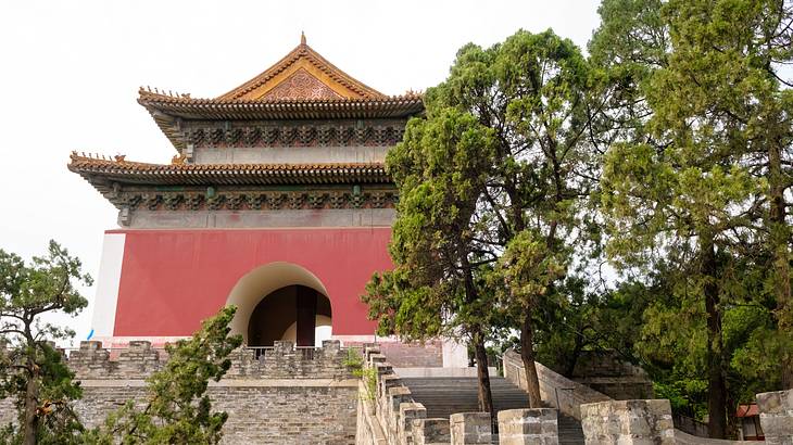 A stone walkway leading to a red-walled historical building with trees around it