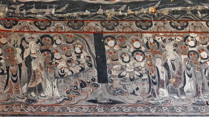 A cave wall painted with a picture of praying monks with halos