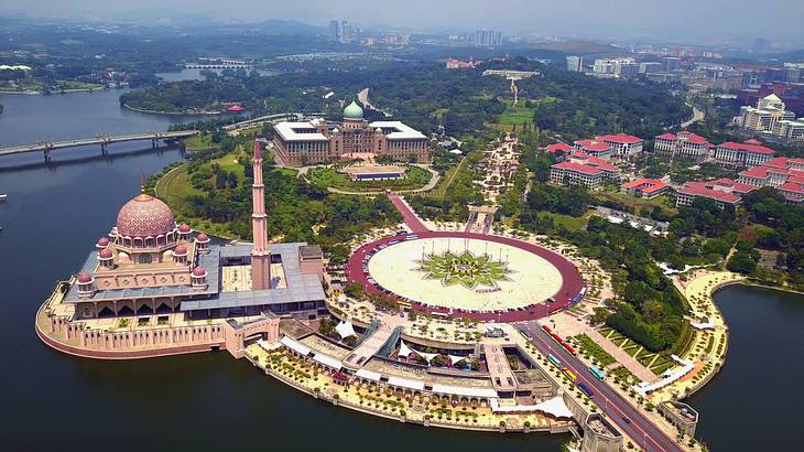 An aerial view of a vast, pink-colored mosque and greenery next to a lake