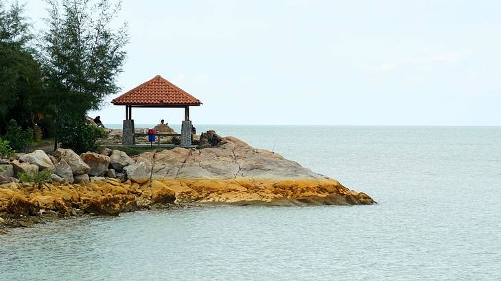 A pavilion on a rocky shoreline with greenery on the left and surrounded by the sea