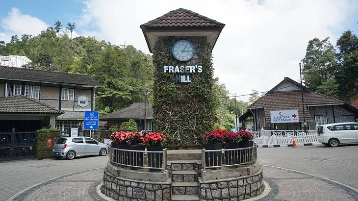 A clock tower with flowers and greenery and a "Fraser's Hill" sign