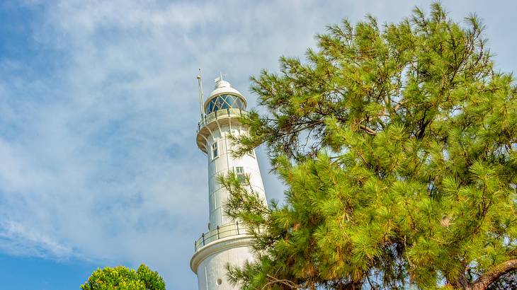 A white lighthouse in between two trees under a partially cloudy sky