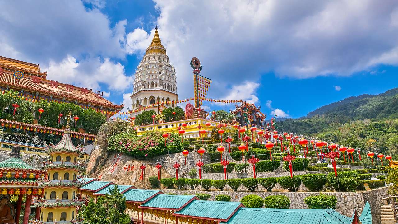 A temple with colorful decorations next to green hills and a blue sky with clouds