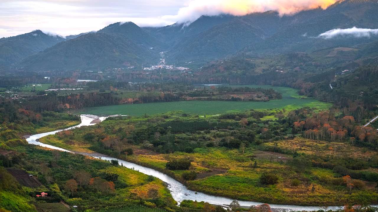 An aerial view of the valley with a long river, greenery, and mountains in the back