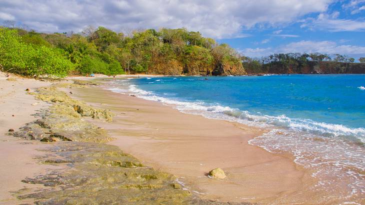 A sand beach with turquoise water and a cliff in the background