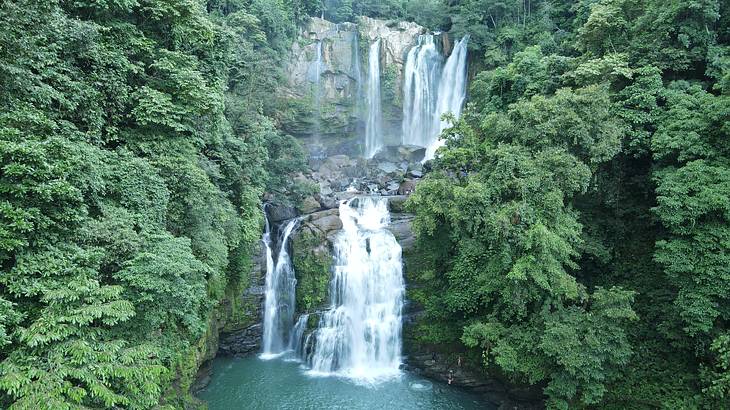 An aerial view of waterfalls in the middle of the jungle surrounded by lush greenery