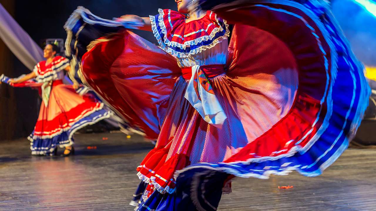 Female dancers in traditional costumes with red, blue, and white on the stage