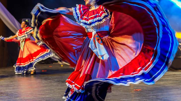 Female dancers in traditional costumes with red, blue, and white on the stage