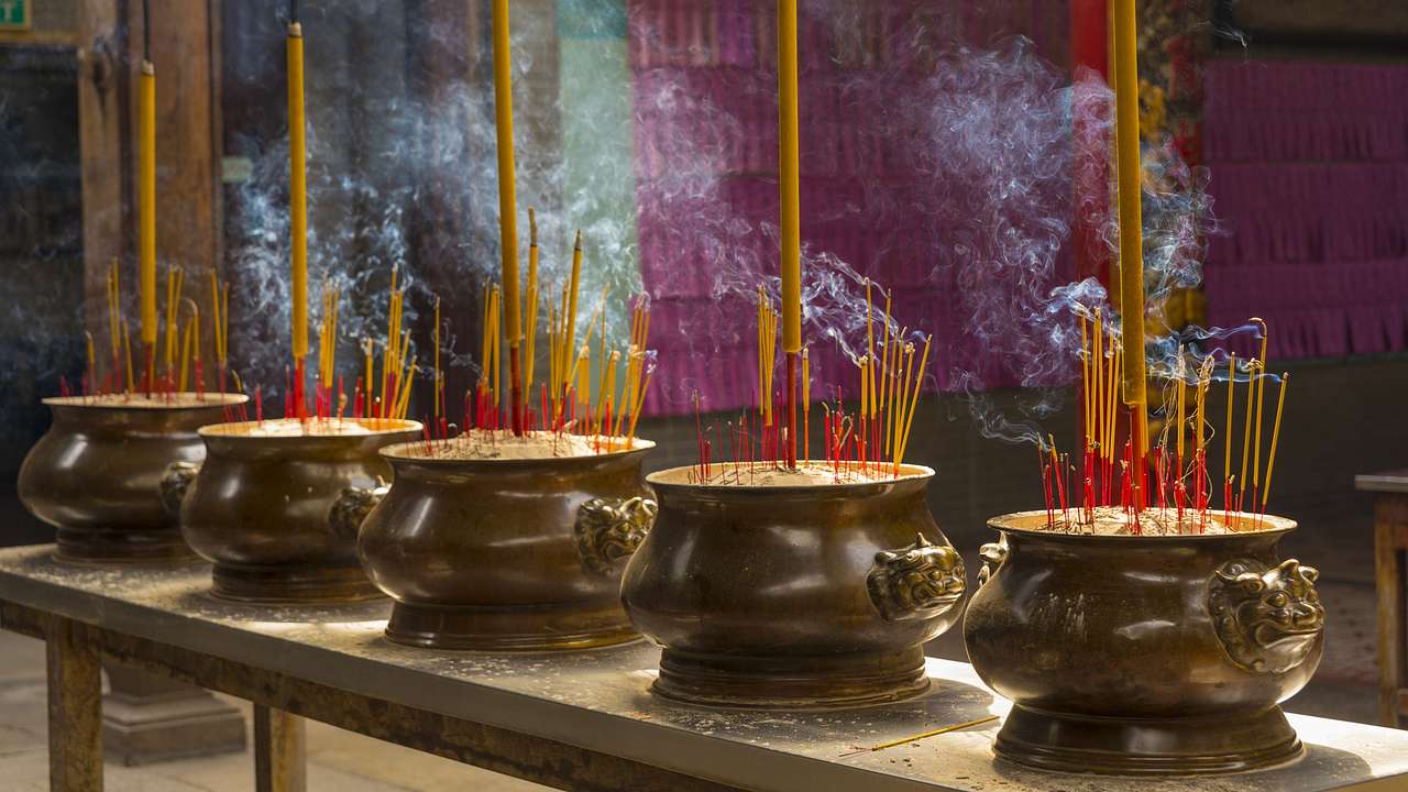 Incense sticks burning on five brown metal pots placed on a table