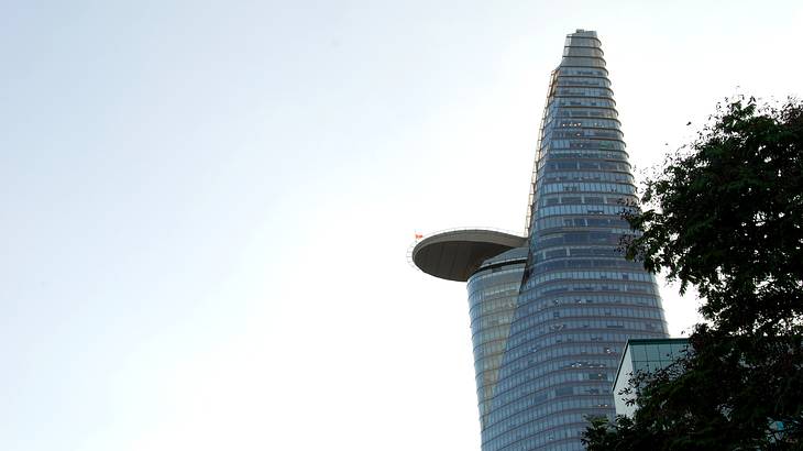 A tall glass tower with a protruding deck and a tree to its left