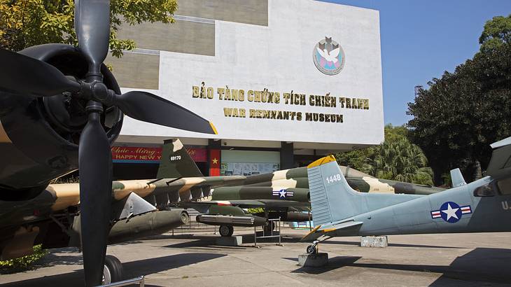 A building with a sign in Vietnamese and English and warplanes displayed in front