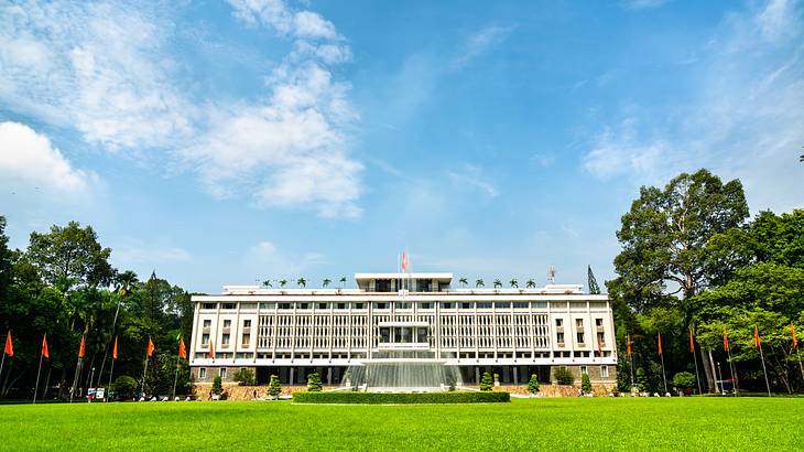 A building with flags, and a fountain in front, surrounded by grass and trees