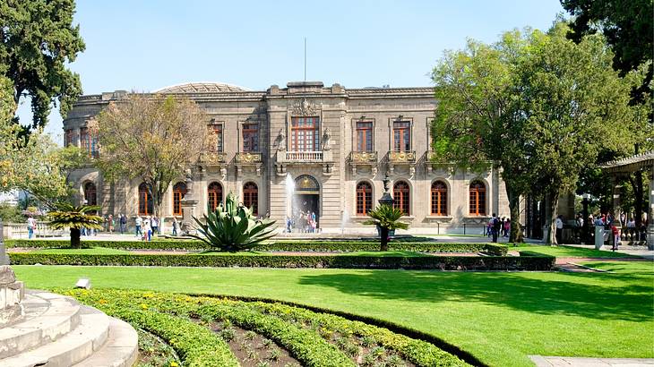 A stone palace-style building with green grass and trees in front of it