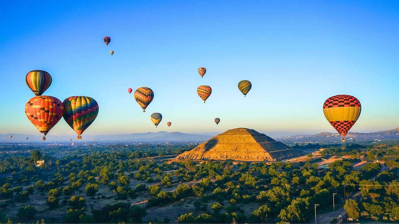 An ancient pyramid structure with colourful hot air balloons flying above it
