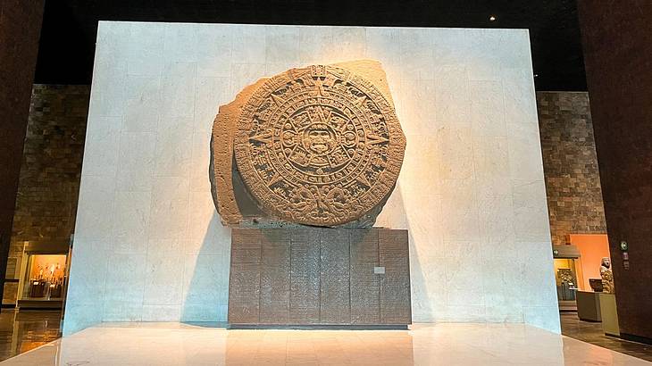 A massive white stone wall with an ancient Aztec sundial on a large stand in front